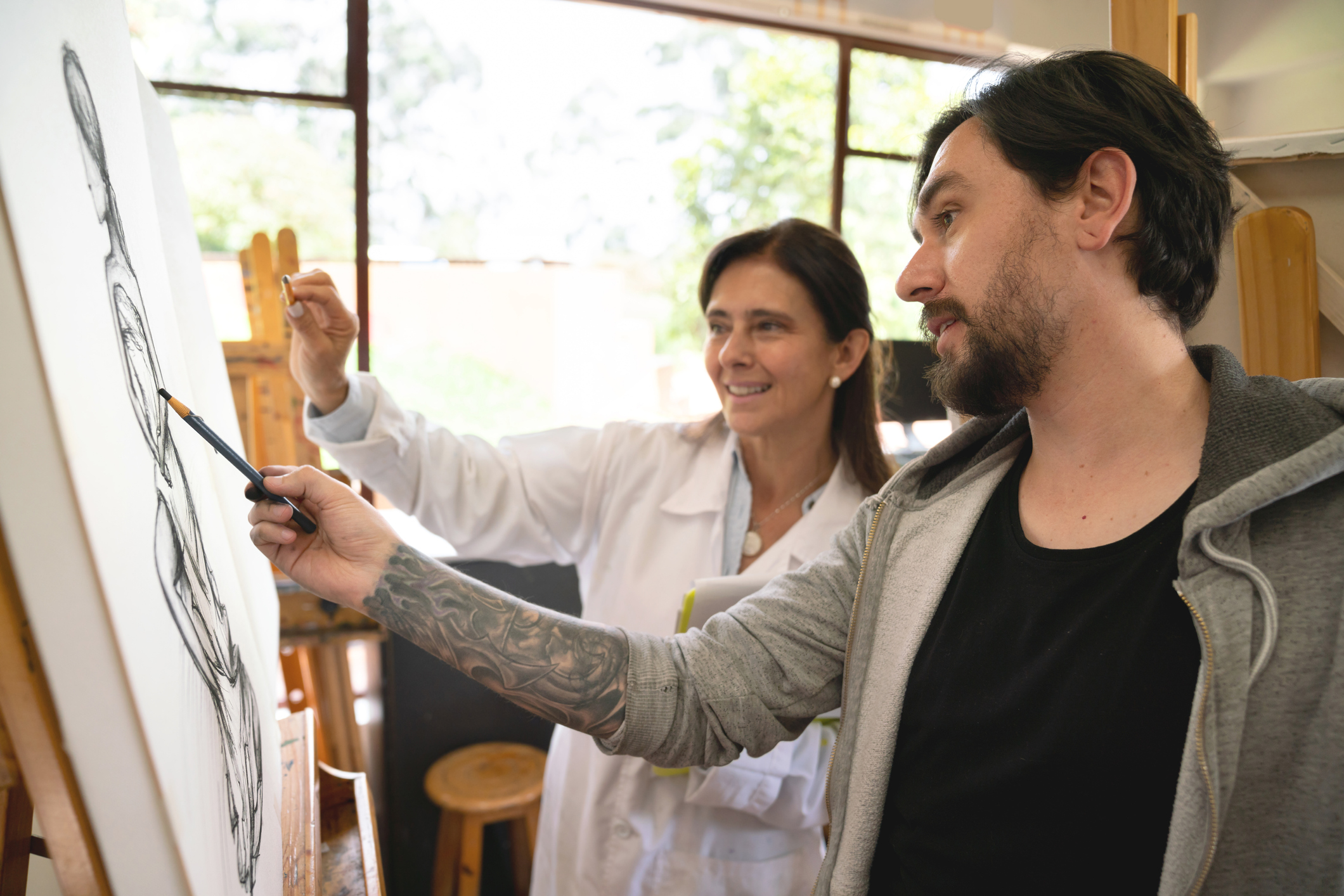 Man in an art class painting and talking to the teacher